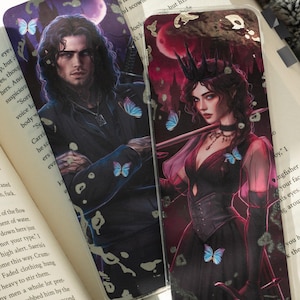 Può includere: Due custodie per telefono con arte fantasy. Una raffigura un uomo con lunghi capelli scuri e farfalle. L'altra raffigura una donna con una corona, che tiene una spada, e ha anche farfalle. Entrambe le custodie hanno uno schema di colori scuri.