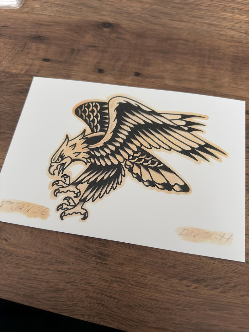 May include: A black and tan eagle illustration on white paper. The eagle is depicted with outstretched wings and sharp talons. The artwork is signed "DAVID-H" and dated "5th JAN 26".
