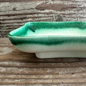 May include: A rectangular ceramic dish with a gradient of green and white glaze. The dish has a curved shape with a raised base. The glaze transitions from a deep green at the rim to a soft white at the base.
