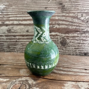 May include: A green ceramic vase with a textured surface and a flared top. The vase features white zigzag and rectangular patterns around the neck and base. The vase is approximately 6 inches tall.