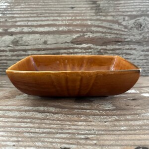 May include: A rectangular, brown ceramic bowl with rounded corners. The bowl has a glossy finish and a slightly textured surface. The interior of the bowl is a lighter shade of brown than the exterior. The bowl is empty and sits on a wooden surface.