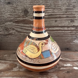 May include: Hand-painted ceramic vase with a bulbous body and a narrow neck. The vase features a design of yellow ducks, colorful geometric shapes, and the word "Mexico". The neck has alternating bands of black, white, and orange.