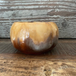 May include: A brown and cream glazed ceramic planter with a rounded shape. The planter has a mottled glaze with brown, cream, and white tones.