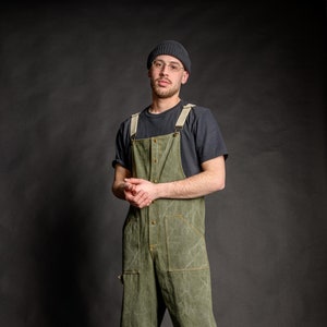 Barista wearing comfortable unisex streetwear salopette, which has adjustable cotton beige straps with dungaree metal clip fasteners.