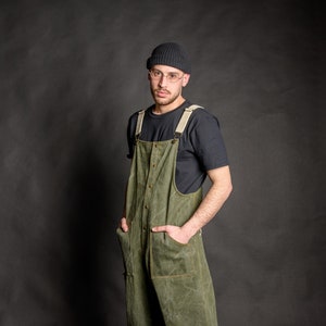 Young man wearing his olive green baggy overall, made from high quality cotton fabric, with metal bronze stud buttons and two front pockets.