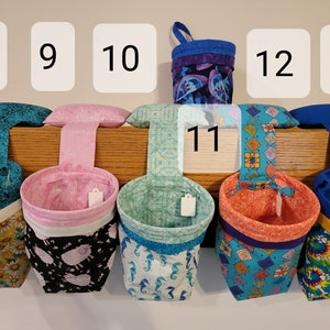 May include: Six hanging fabric storage bins with different patterns and colors. The bins are numbered 8 through 13. The bins are hanging from a wooden shelf.