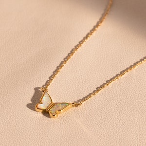 May include: A delicate gold chain necklace with a small opal butterfly pendant.