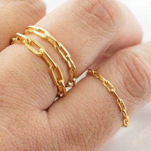 May include: Gold-colored chain link rings. The rings are worn on a hand, with two rings on one finger and a single ring on another. The rings have a bright, shiny finish and a classic, elegant design.