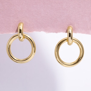 May include: A pair of gold hoop earrings with a simple, circular design. The earrings are made of thick, polished metal and have a smooth, shiny finish.