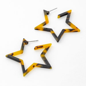 May include: A pair of star-shaped hoop earrings made of brown and yellow tortoiseshell-patterned plastic.