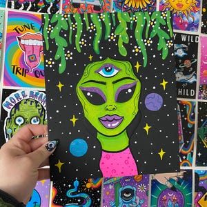 May include: A psychedelic art print featuring a green alien with a third eye on its forehead. The alien has pink lips and purple eyeshadow. The background is black with white stars and a blue planet.