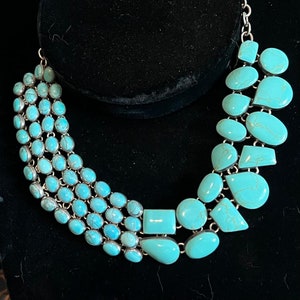 May include: A turquoise and silver statement necklace with multiple strands of oval-shaped turquoise stones and a cascading design of larger, irregularly shaped turquoise stones.
