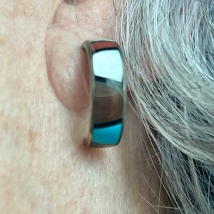 Puede incluir: Un aro de plata para la oreja con una incrustación multicolor. La incrustación presenta colores turquesa, marrón, blanco y rojo.