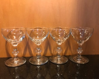 May include: Four clear glass stemmed drinking glasses with a rounded bowl shape. The glasses are arranged in a row on a black surface.