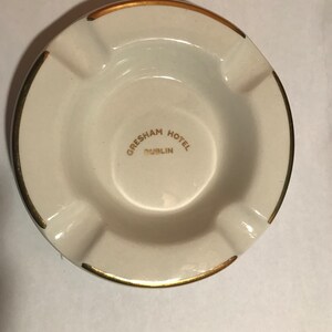 May include: White ceramic ashtray with a gold rim and the words "Gresham Hotel Dublin" in gold lettering.