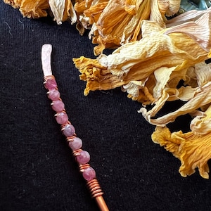 Può includere: Un bastoncino per capelli avvolto in filo di rame con perline di pietre preziose rosa e bianche.