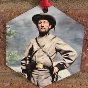 May include: Hexagon-shaped ornament featuring a colorized portrait of a man in a Civil War uniform, complete with a hat and cross-body straps. The ornament is suspended by a red ribbon, perfect for holiday decor or historical enthusiasts.