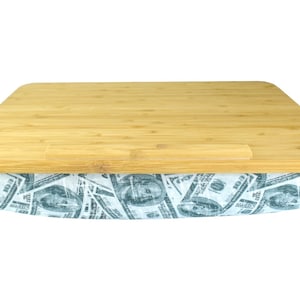 Puede incluir: Un escritorio para portátil de bambú con una base acolchada con un patrón de billetes de dólar estadounidenses. El escritorio tiene un borde elevado para evitar que los objetos se deslicen.