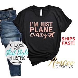 May include: Black t-shirt with the text "I'm just plane crazy" in rose gold lettering and a small airplane graphic. The shirt is shown on a model wearing blue jeans.