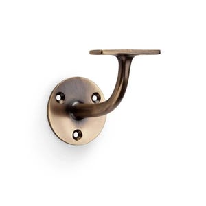 May include: A bronze-toned metal handrail bracket featuring a circular wall-mounting plate with three screw holes and a curved support arm extending to a flat, horizontal top plate designed to hold a railing securely in place.