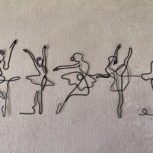 May include: Five black wire sculptures of ballerinas in various poses. The ballerinas are all in a line, with their arms outstretched and their legs in a graceful position.