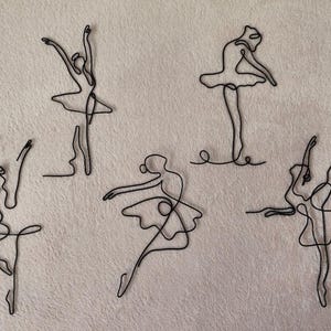 May include: Five black wire sculptures of ballerinas in various poses. The sculptures are made of thin wire and are delicate in appearance.