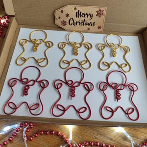 May include: Six wire-wrapped gingerbread man ornaments, three gold and three red, in a cardboard box with a "Merry Christmas" sign.