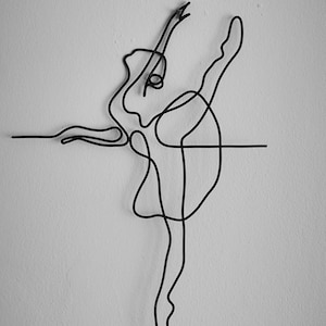 May include: A black wire sculpture of a ballerina in a pose with one leg extended. The sculpture is mounted on a white wall.