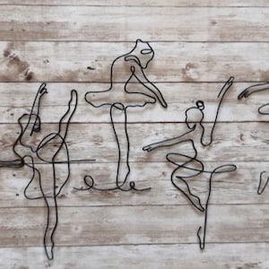 May include: Five black wire sculptures of ballerinas in various poses on a wood background.