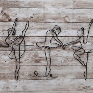 May include: Five black wire sculptures of ballerinas in various poses on a wood background.