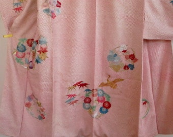 May include: A light pink kimono with embroidered floral and bird designs. The kimono features detailed embroidery of flowers, leaves, and a crane in shades of red, blue, green, and gold. The fabric has a subtle dotted texture.