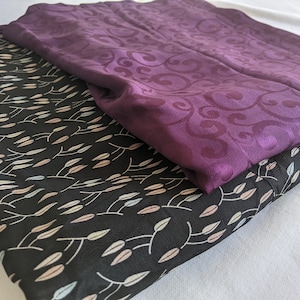 Peut inclure: Deux morceaux de tissu, l'un noir avec un motif de feuilles blanches et bleu clair et l'autre violet avec un motif en spirale.