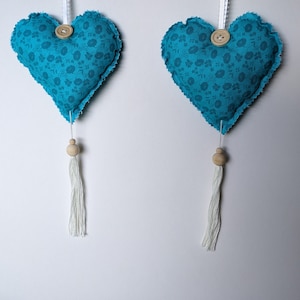 May include: Two blue fabric heart-shaped ornaments with white floral patterns and wooden beads hanging from white strings.