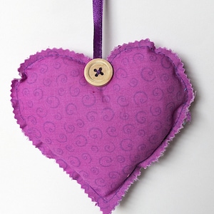 May include: Purple fabric heart with a swirl pattern and a wooden button. The heart is attached to a purple ribbon.