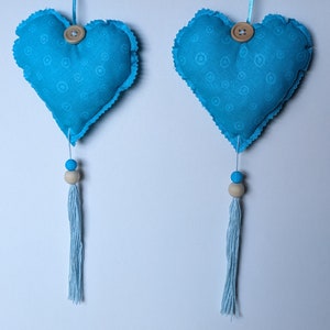 May include: Two blue fabric hearts with white polka dots and wooden buttons hang from blue tassels. The hearts are attached to white string.