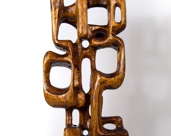 Könnte beinhalten: Eine hohe, abstrakte Holzskulptur mit warmbraunem Finish. Das Kunstwerk zeigt eine Reihe miteinander verbundener, geometrischer Formen mit offenen Räumen, die ein einzigartiges und strukturiertes Aussehen erzeugen. Die Skulptur steht aufrecht vor einem weißen Hintergrund.