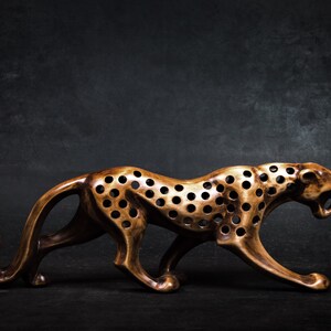 May include: A wooden cheetah figurine with a brown finish and a spotted pattern. The figurine is carved with holes throughout the body, creating a unique and intricate design.