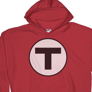 Może przedstawiać: Czerwona bluza z kapturem z białym kołem i czarną literą "T" w środku.