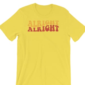 May include: Yellow short-sleeved t-shirt with the text "Alright Alright" in a retro font with red and orange accents.