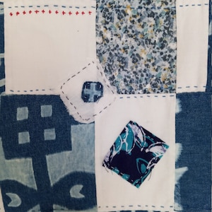 Pode incluir: Um edredom de retalhos de tecido branco com quadrados de tecido com padrões azuis e brancos. O edredom é costurado com fio azul e vermelho.