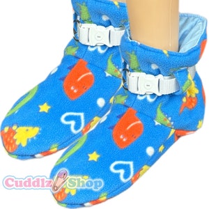 May include: Blue fleece baby booties with a dinosaur and heart print. The booties have adjustable white straps with a buckle closure.