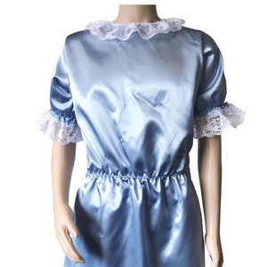 Peut inclure: Une robe en satin bleu clair avec une bordure en dentelle blanche autour du col, des manches et de l'ourlet. La robe a une taille froncée et un logo Cuddly Shop sur le devant.