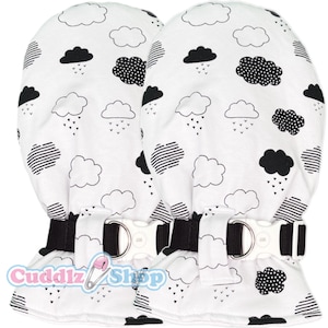 May include: Two white baby mittens with a black and white cloud pattern. The mittens have a black strap with a white buckle. The text "Cuddlz Shop" is printed on the bottom of the mittens.
