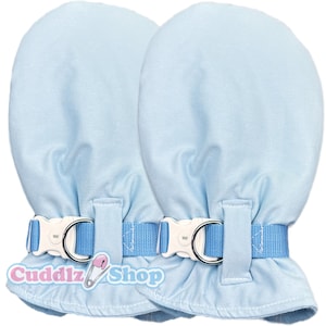 Può includere: Un paio di guanti da bambino azzurri. Ogni guanto ha una fibbia di plastica bianca con un cinturino blu e un anello di metallo argentato. La parte inferiore dei guanti ha un bordo a balze. Il testo "Cuddlz Shop" è stampato in basso.