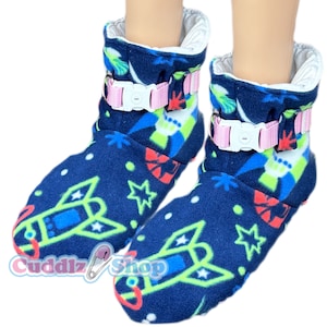 May include: A pair of blue fleece slipper booties with a rocket ship and star print. The booties have pink and white adjustable straps with buckles.