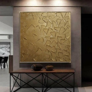 Puede incluir: Pintura abstracta dorada con una superficie texturizada y en relieve. La pintura está enmarcada y colgada en una pared en un interior moderno.