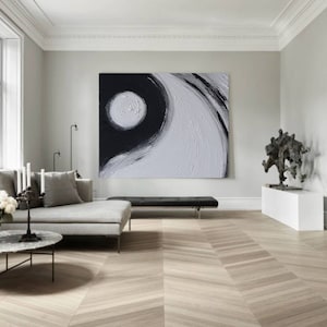 May include: A black and white abstract painting with a large white circle in the center. The painting is hanging on a white wall in a modern living room.