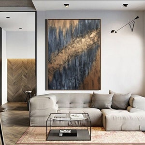 May include: Abstract painting with gold and blue hues on a canvas. The painting is hanging on a wall in a living room with a couch and coffee table.
