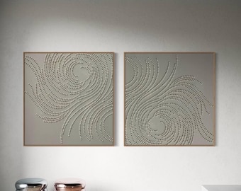 May include: Two framed wall art pieces with a spiral dot design in a neutral color. The artwork is displayed on a white wall, with two metallic accent stools in the foreground. The stools are silver and rose gold.