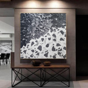 Puede incluir: Pintura abstracta en blanco y negro sobre lienzo con un estilo moderno. La pintura se muestra en una pared sobre una mesa de madera con un marco de metal negro.